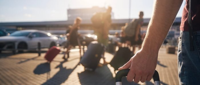 Group of people walking to airport terminal at summer sunset. Selective focus on hand of man with suitcase.